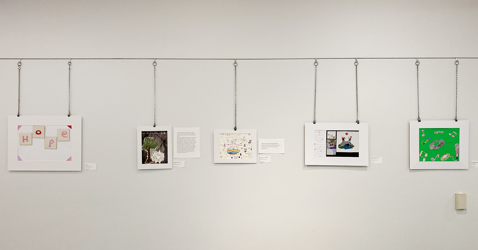 White wall in the Rotary Room at Main Branch with five pieces of artwork.