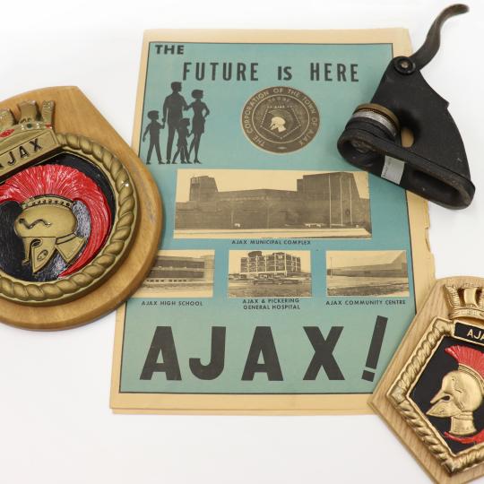 Objects from the Ajax Archives including two crests with Trojan style helmets, an embossing press, and a business brochure from the 1950s. 