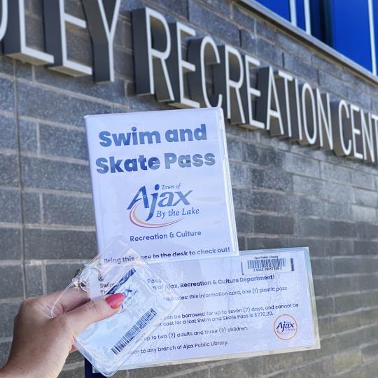 A person holding a Town of Ajax Swim and Skate pass in front of a brick wall at Audley Recreation Centre.